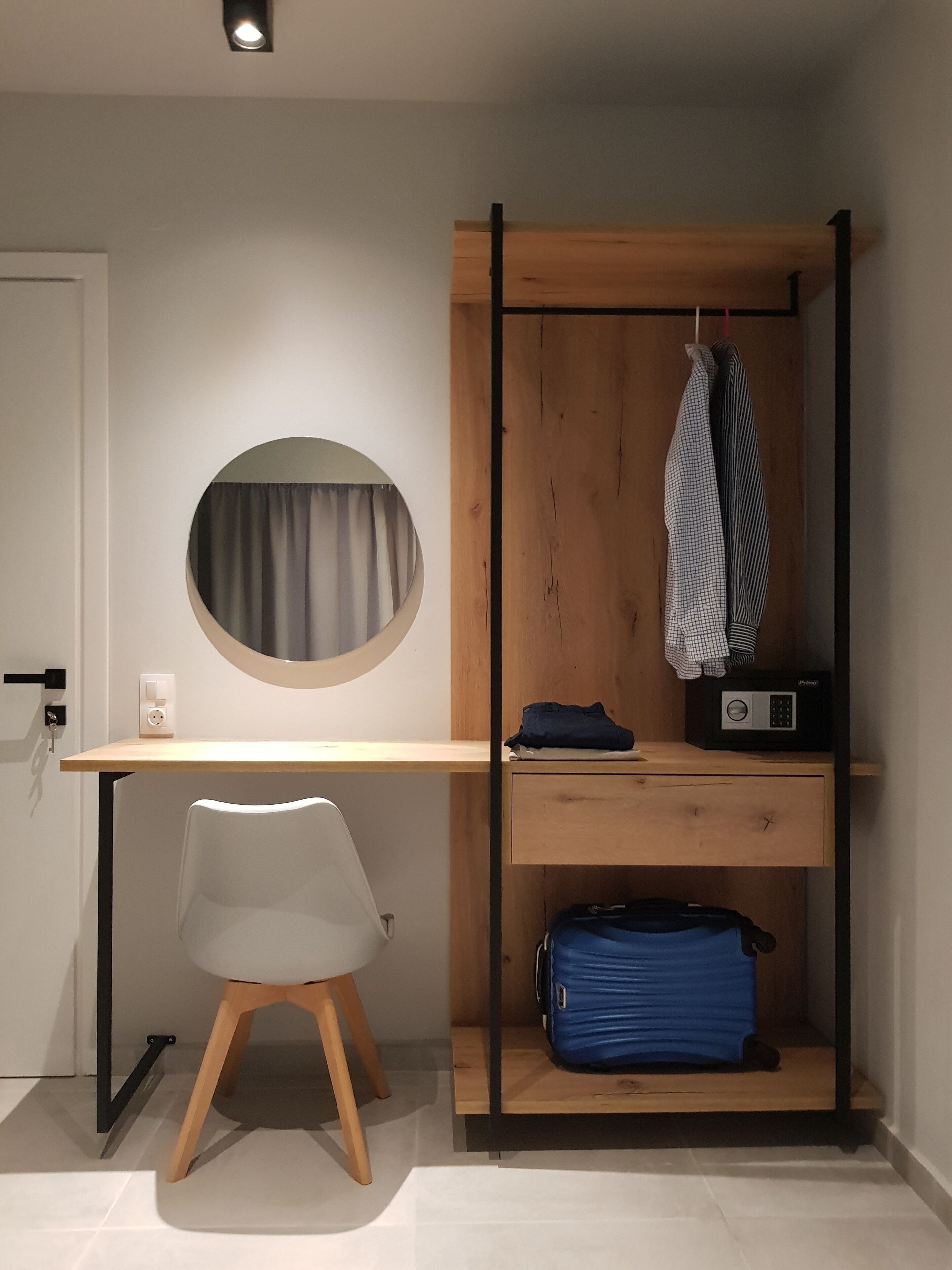 A compact room with a desk, chair, and a built-in wardrobe with hanging clothes and a radio.
