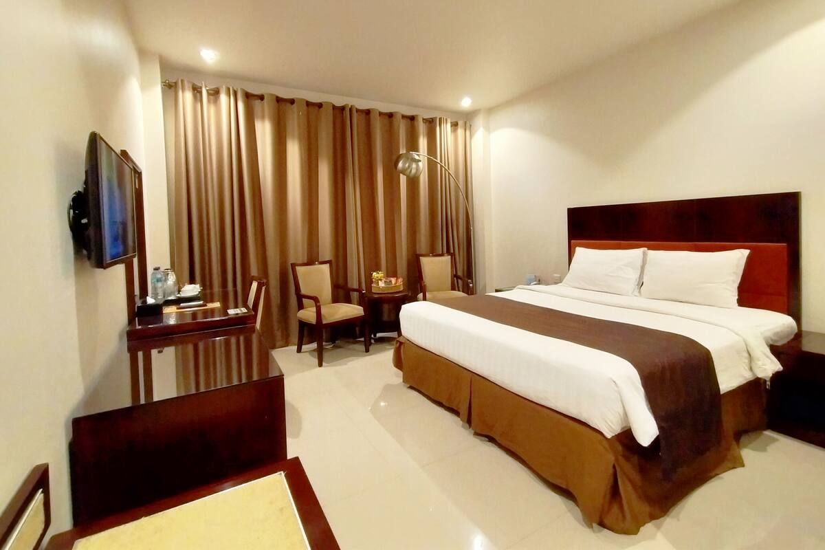 A hotel room with a large bed, a desk with a chair, a TV, and a window with curtains.