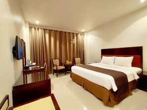 A hotel room with a large bed, a desk with a chair, a TV, and a window with curtains.