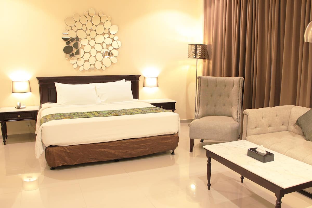 A hotel room with a large bed, two bedside lamps, a decorative wall piece, a chair, a sofa, and a small table with a tissue box.