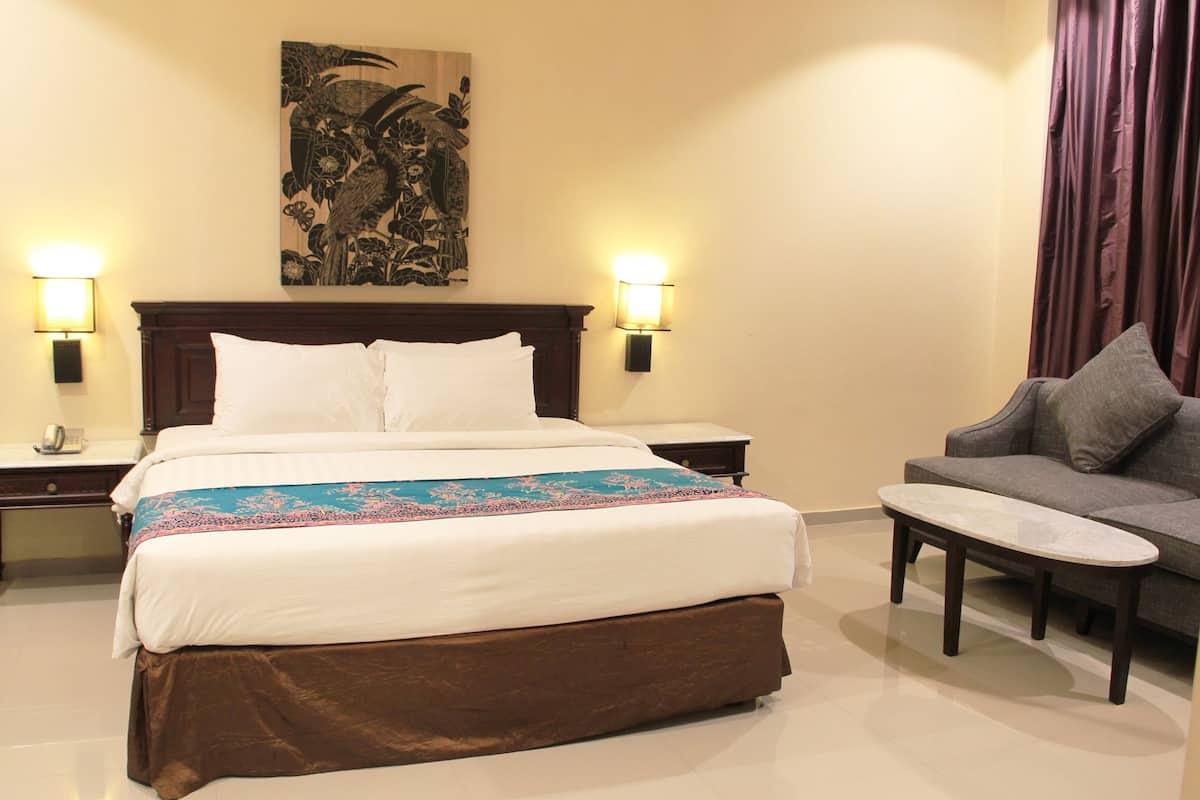 A hotel room with a large bed, two bedside tables, a sofa, and a decorative wall piece.