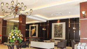 Um hall de entrada com um candelabro, sofás, uma mesa de centro, um arranjo floral e obras de arte nas paredes.