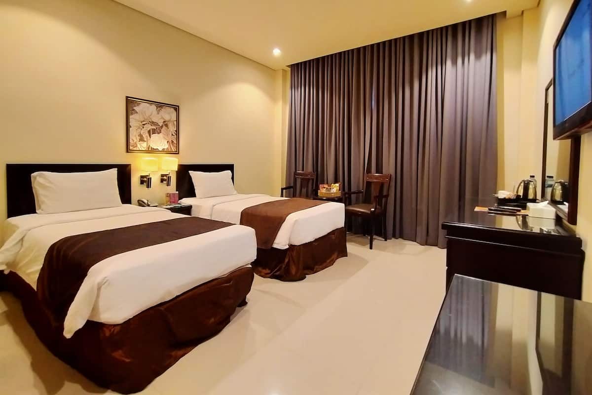 A hotel room with two beds, a desk, a television, and a large window with curtains.
