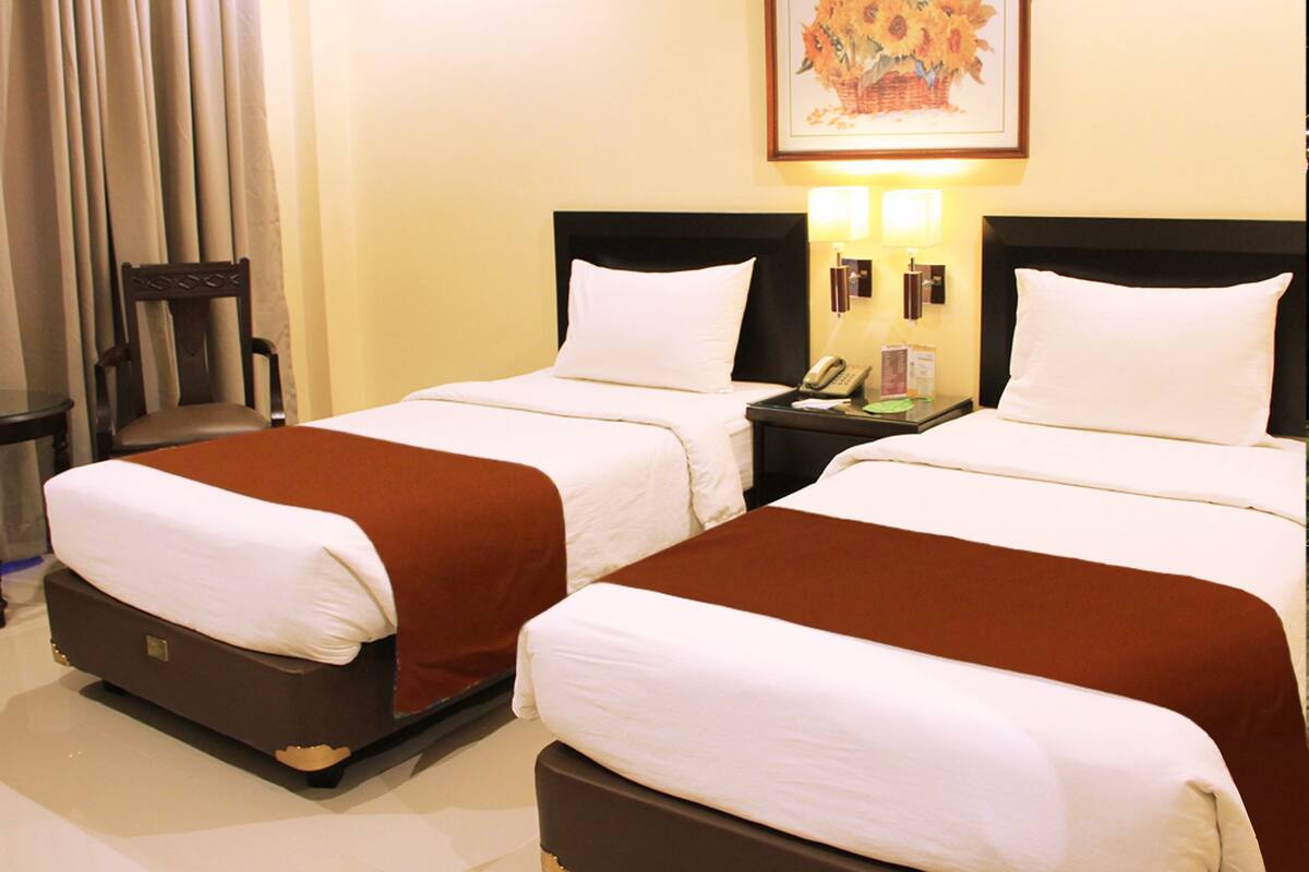 A hotel room with two beds, a chair, a nightstand with a phone, and a framed picture on the wall.