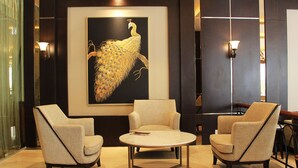Um saguão com três poltronas, uma mesa redonda e uma grande pintura de pavão na parede.