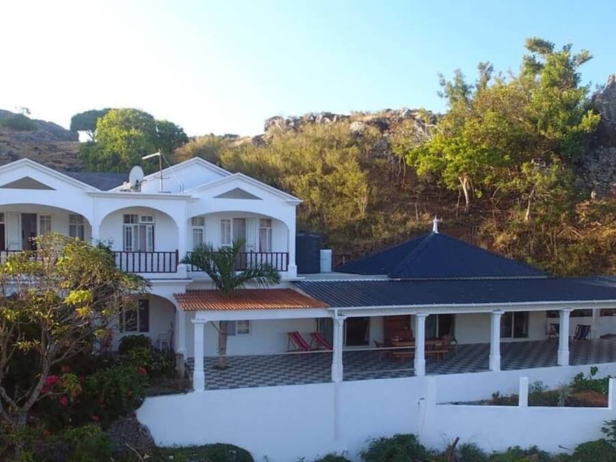 A two-story house with a covered porch and a view of a rocky hillside.