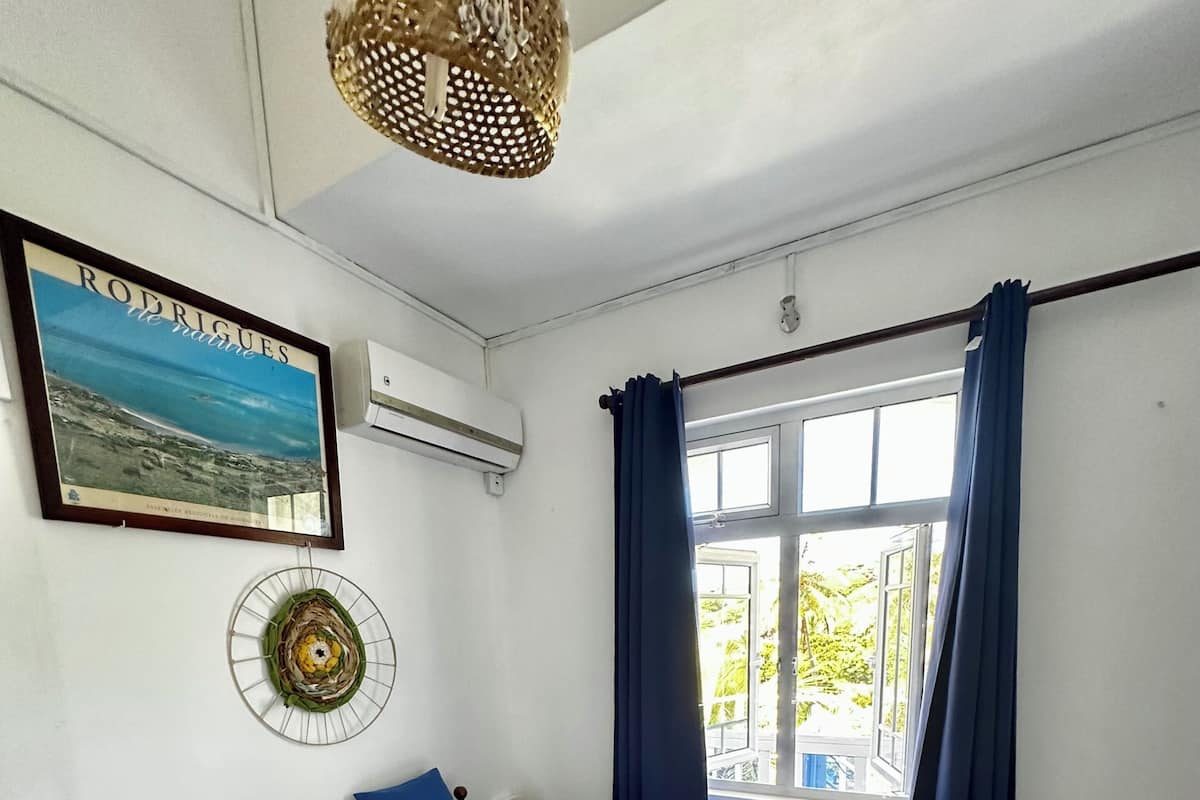 Ein Schlafzimmer mit einem Bett, einer Wand-Klimaanlage, einem gerahmten Bild, einem Fenster mit Vorhängen und einer Pendelleuchte.