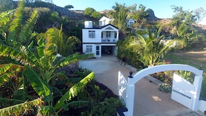 A white two-story house with a balcony, surrounded by lush greenery and a rocky hillside. - La Villa Allamanda (Rodrigues Island)
