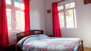 A bedroom with a bed, two windows with red curtains, and a small bedside table.