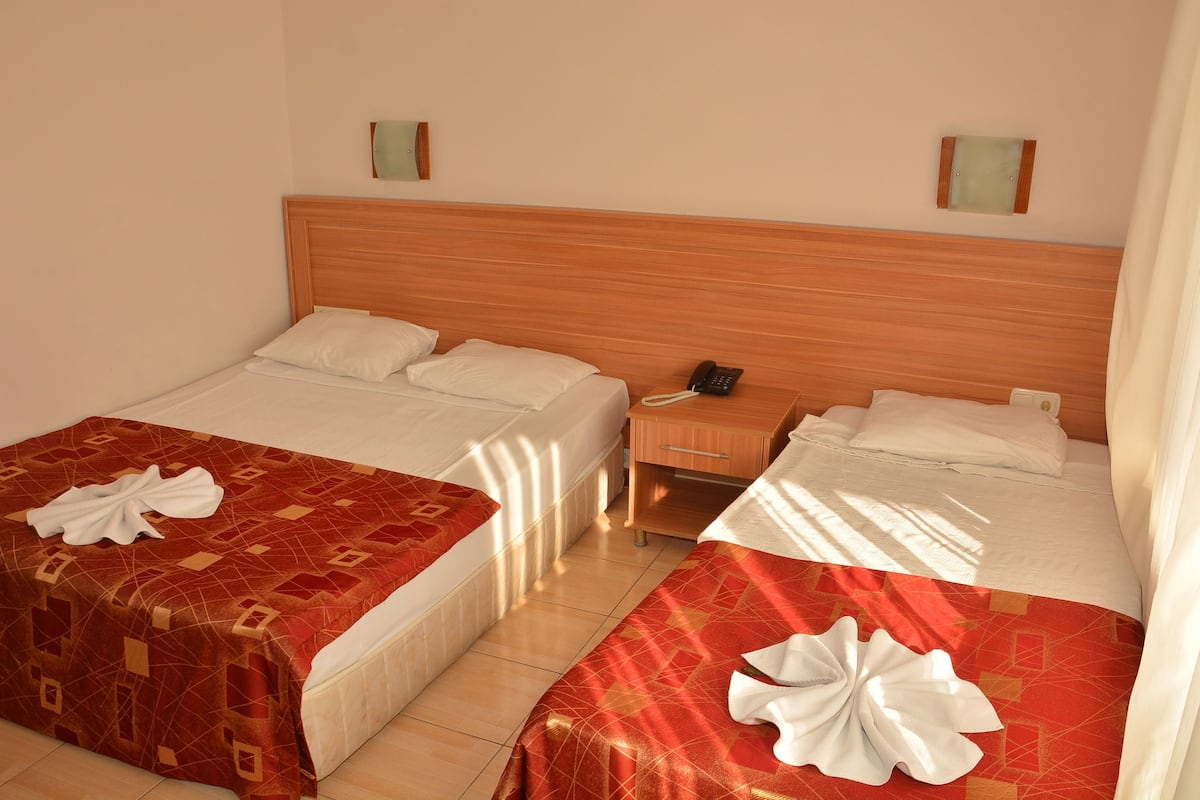 A hotel room with two beds, each with a red and white patterned bedspread and a white pillow. There is a wooden nightstand with a telephone between the beds.