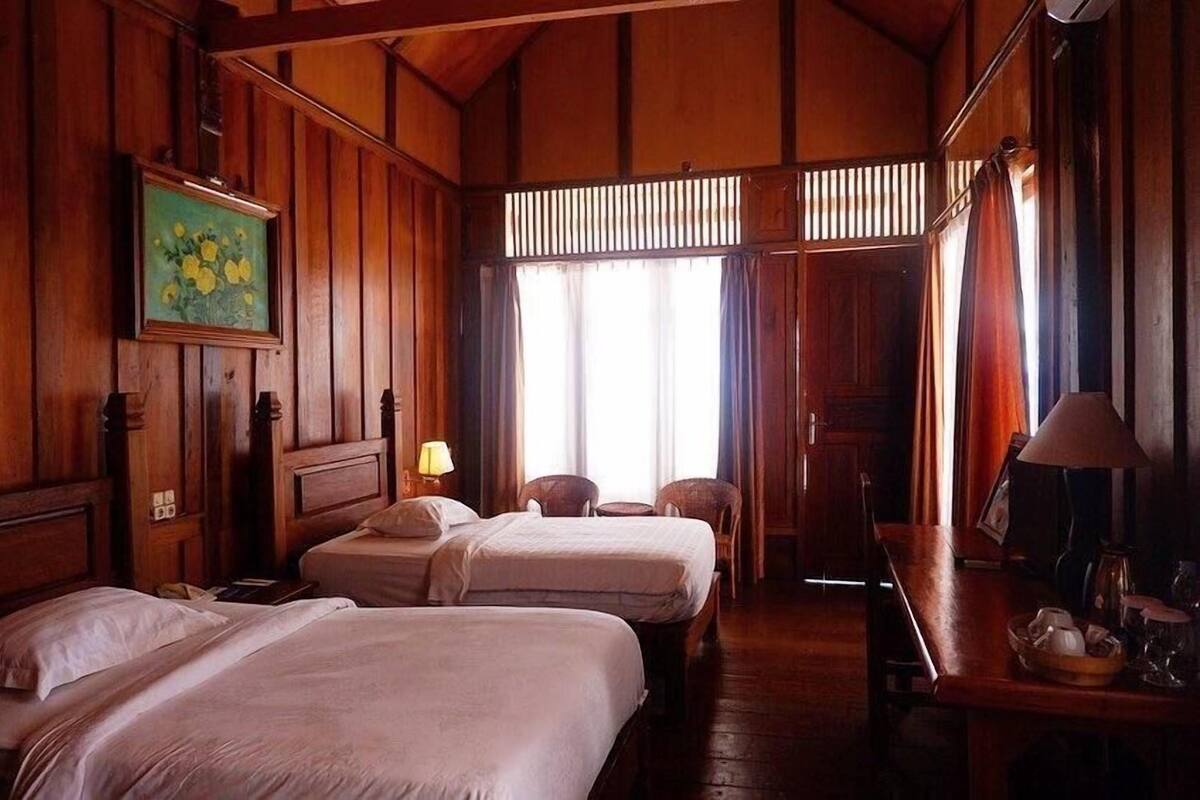 Una habitación con dos camas, una mesa, sillas y un cuadro en la pared.