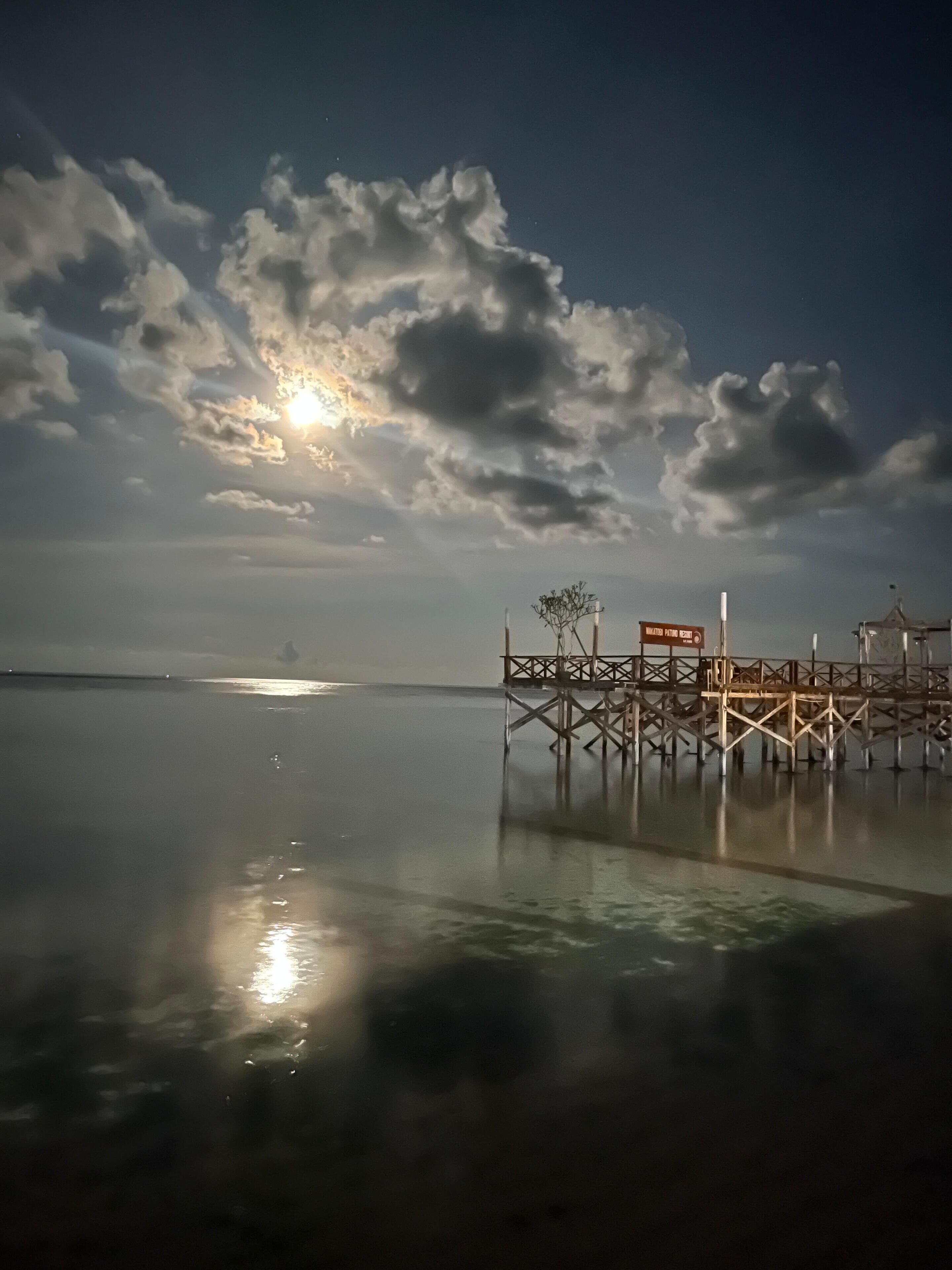 A pier extending into calm water with a clear sky and clouds.