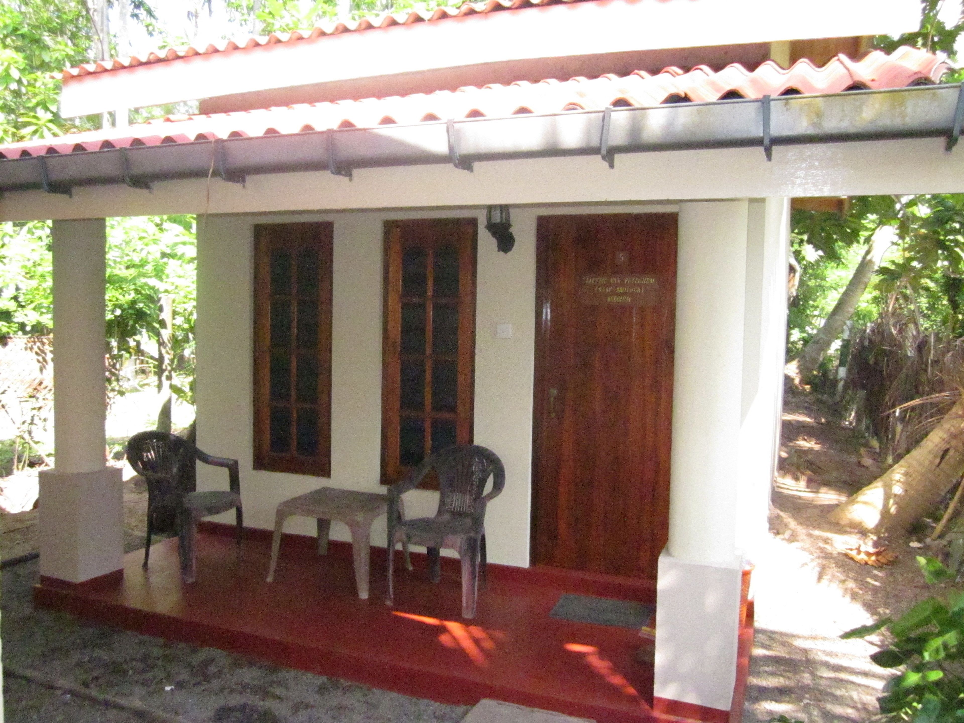 Um pequeno edifício com telhado vermelho e paredes brancas, com duas janelas e uma porta.