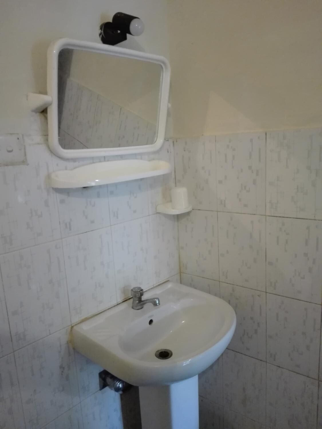 Une salle de bain avec un lavabo blanc, un miroir et un porte-rouleau de papier toilette fixé au mur.