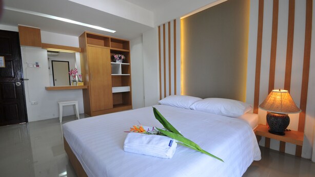 A neatly made bed with a folded towel and flowers, a bedside lamp, and a wooden wardrobe in a hotel room. - Beerapan Hotel (Bangkok)