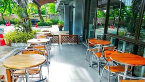 An outdoor seating area with round tables and chairs, surrounded by glass walls with a view of the street. - Beerapan Hotel (Bangkok)