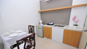 A compact kitchen with a white countertop, a sink, a small refrigerator, and a dining table with plates. - Beerapan Hotel (Bangkok)