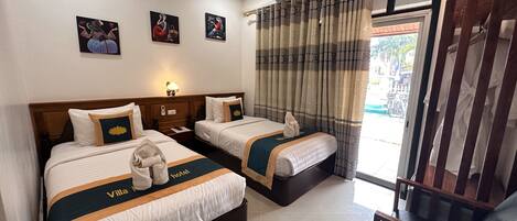 Quarto de hotel com duas camas, uma mesa de cabeceira, uma luminária e vista para o exterior.