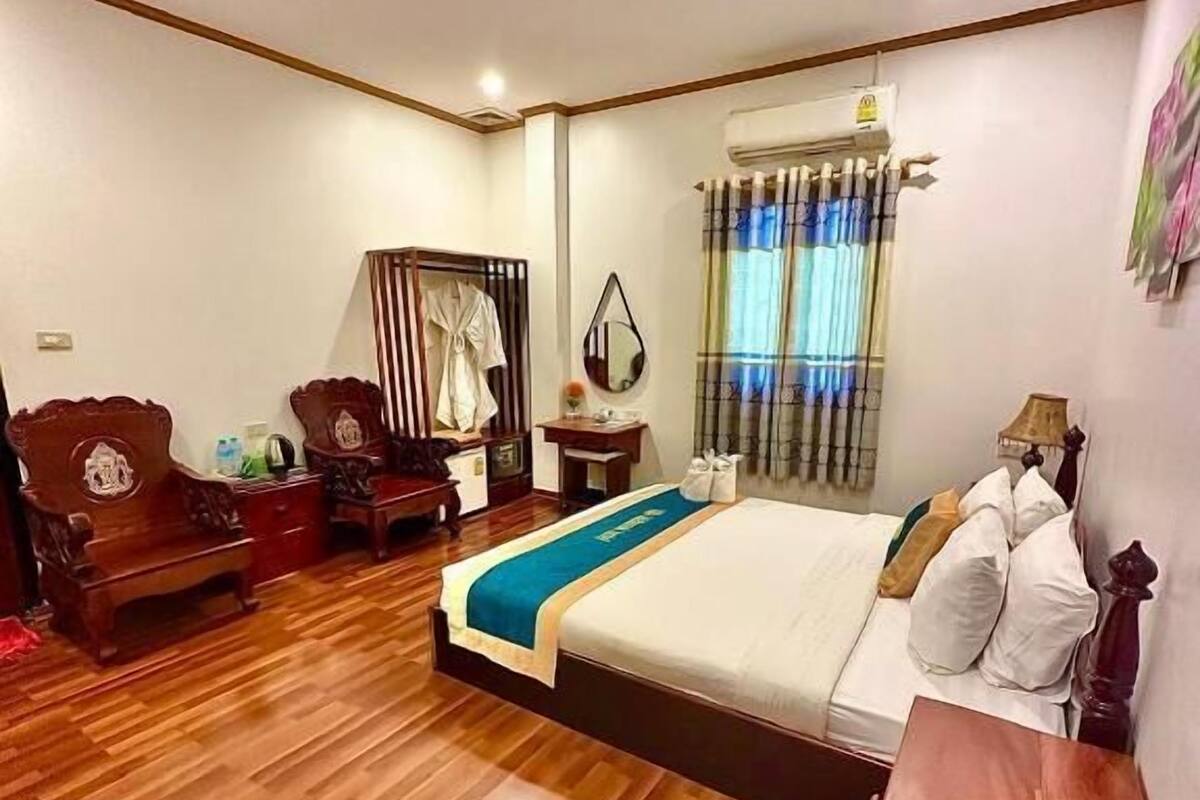 Een slaapkamer met een groot bed, houten meubels, een spiegel en een raam met gordijnen.