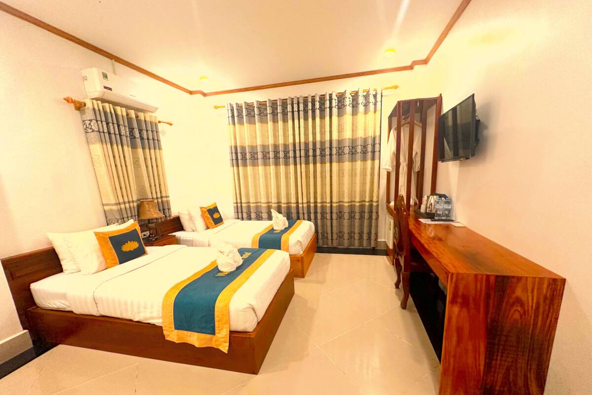 Een hotelkamer met twee bedden, een houten bureau, een flatscreen televisie en een raam met gordijnen.