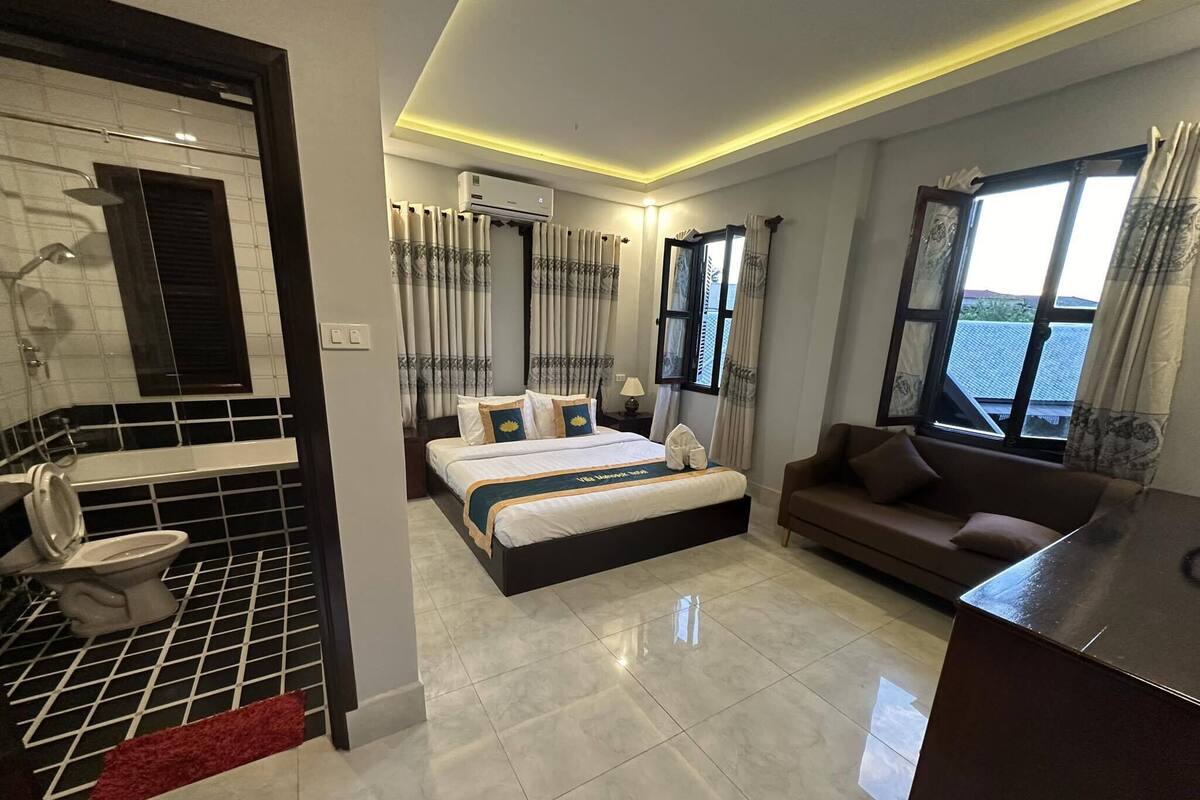 Hotelkamer met een groot bed, een bank, een badkamer met toilet en een raam met uitzicht.