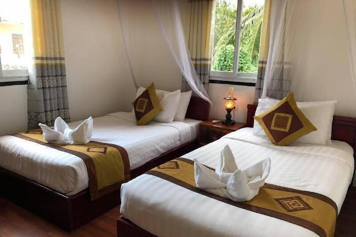 Hotelkamer met twee bedden, elk met een witte spreidek en een bruin hoofdbord, en een raam met uitzicht op groen.