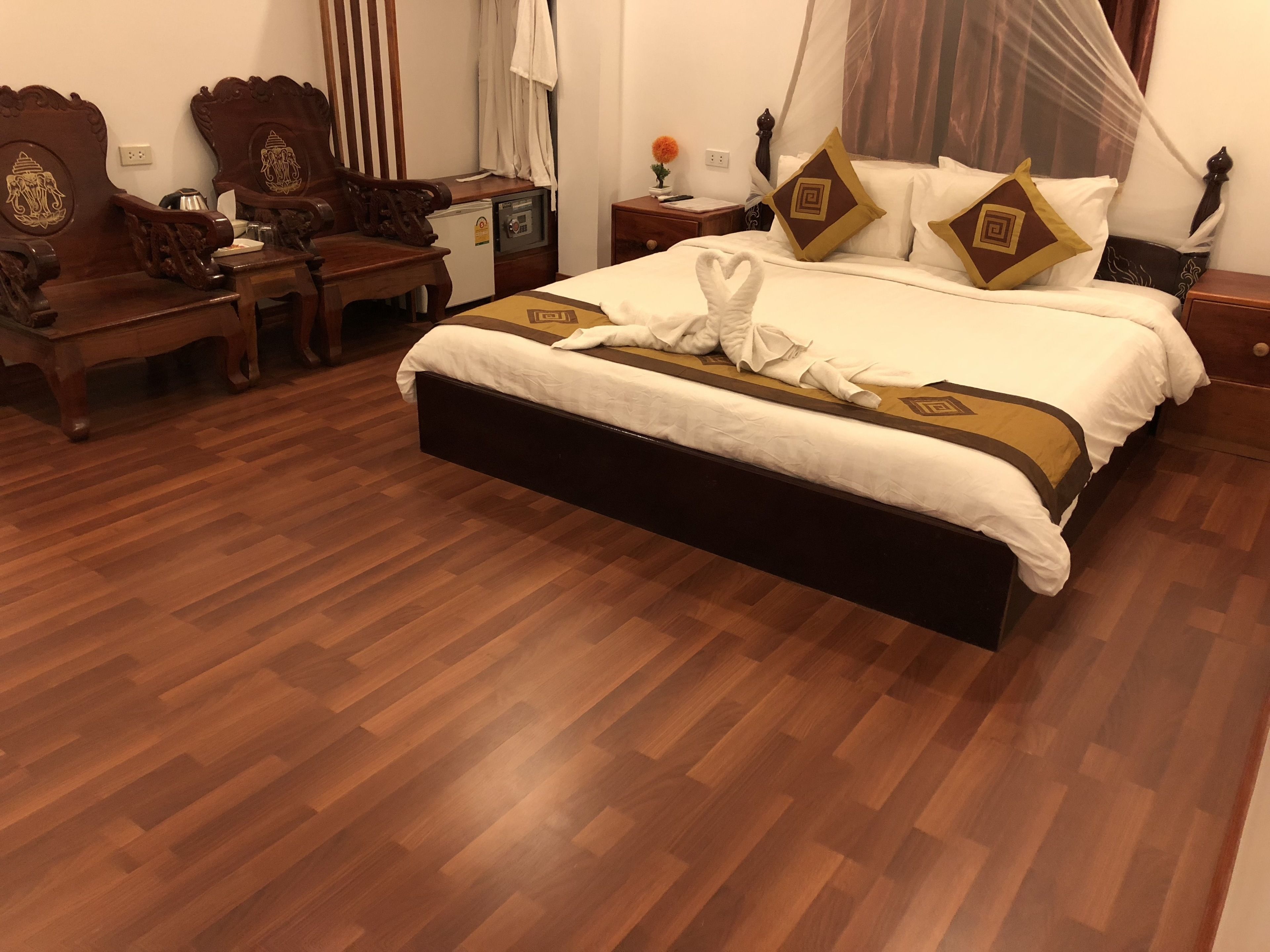 Habitación de hotel con una cama grande, muebles de madera, una caja de seguridad pequeña y una mesita de noche con lámpara.