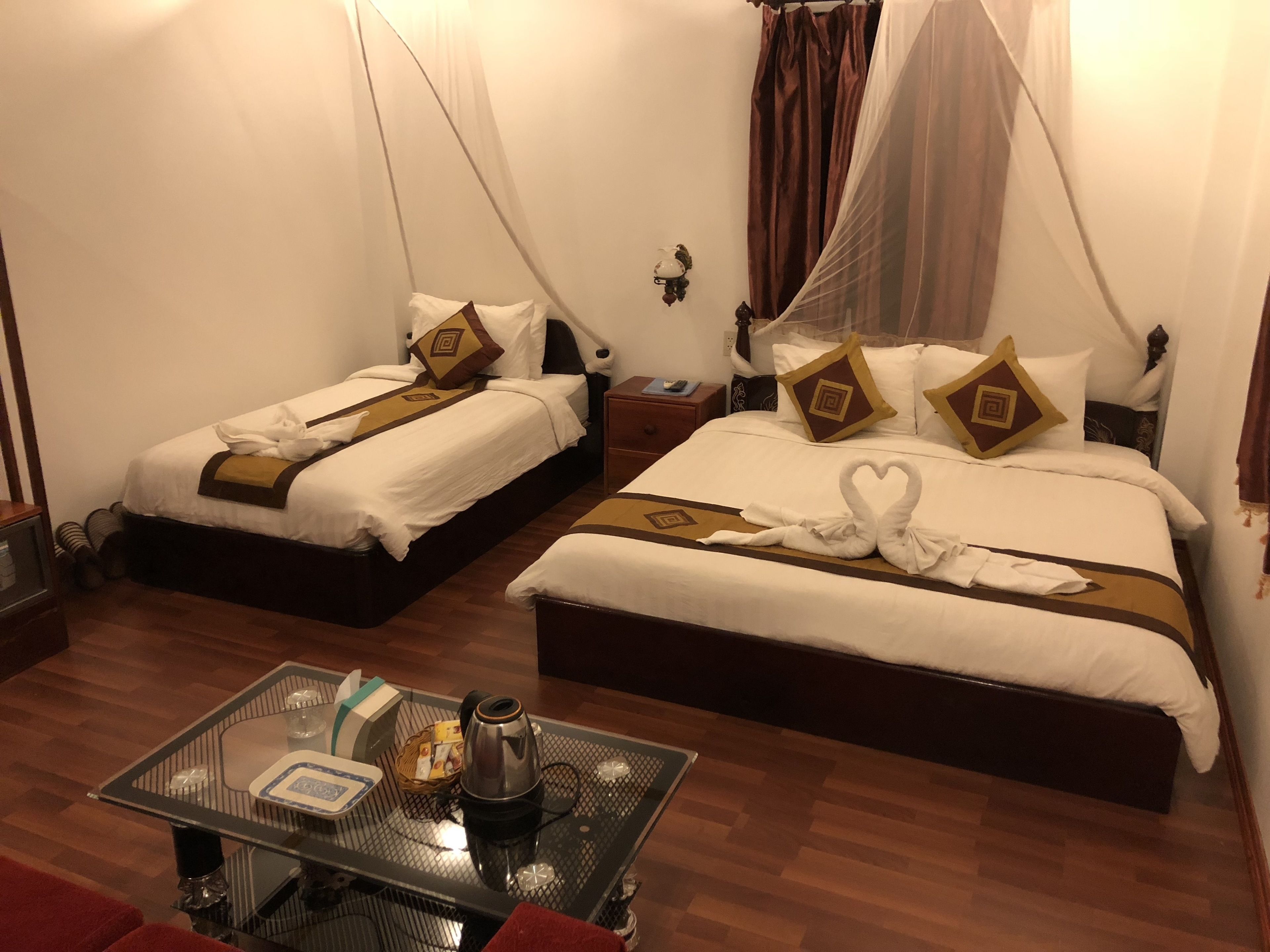 A hotel room with two beds, each with a canopy, and a small table with a kettle and tea set.