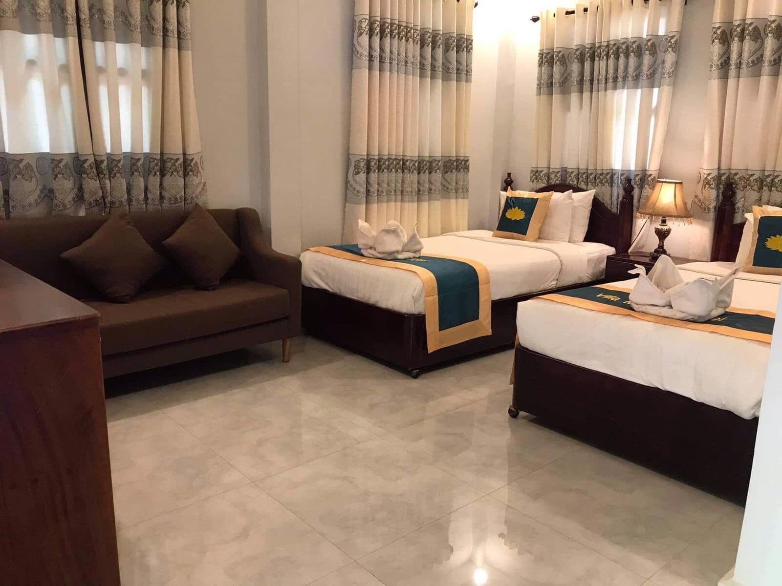 A hotel room with two beds, a sofa, and a lamp.