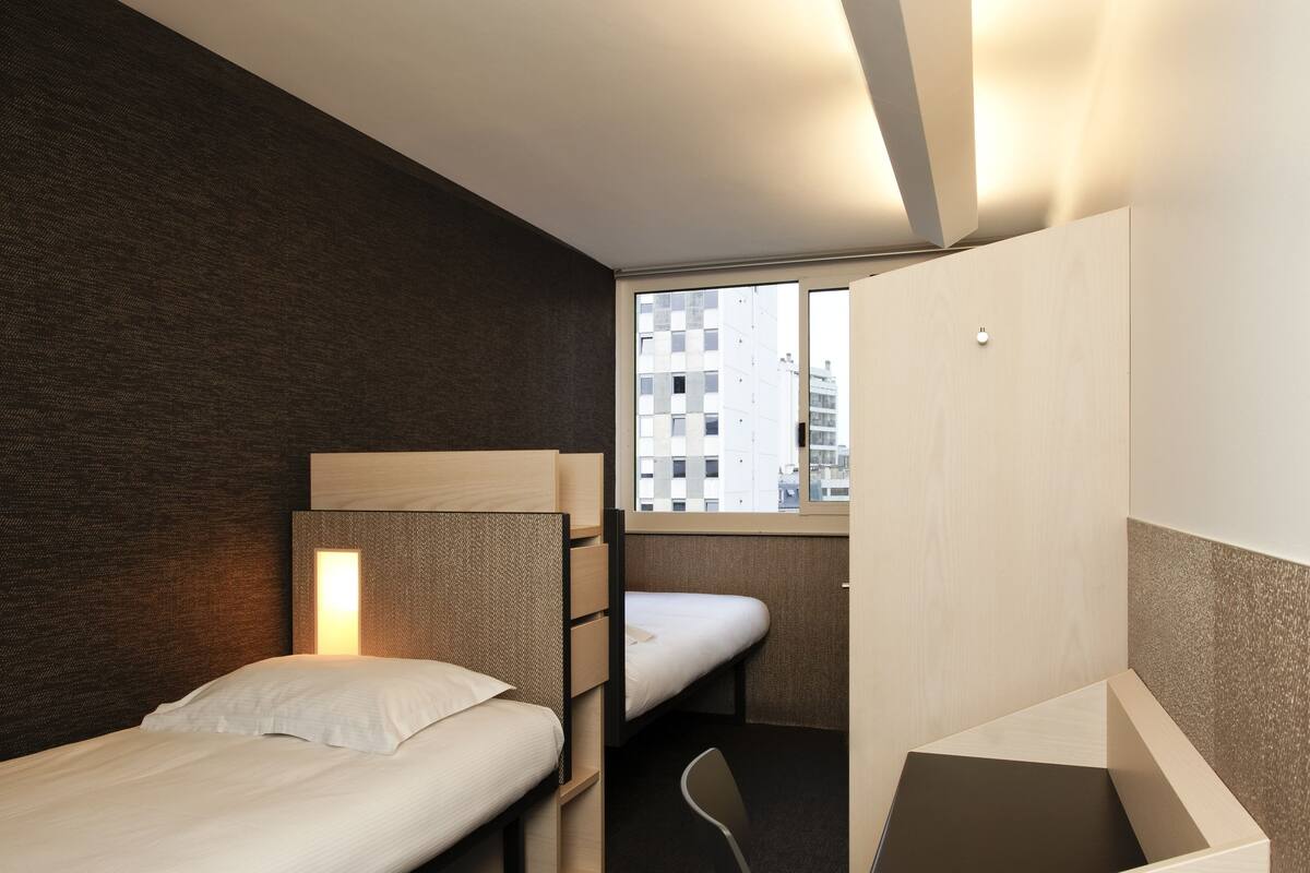 A compact hotel room with two single beds, a desk, and a chair.