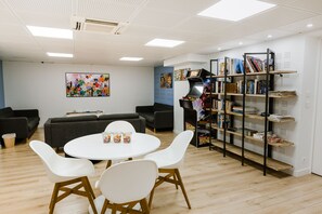 A modern room with a round table, white chairs, a sofa, and a bookshelf. - FIAP - Hostel (Paris)