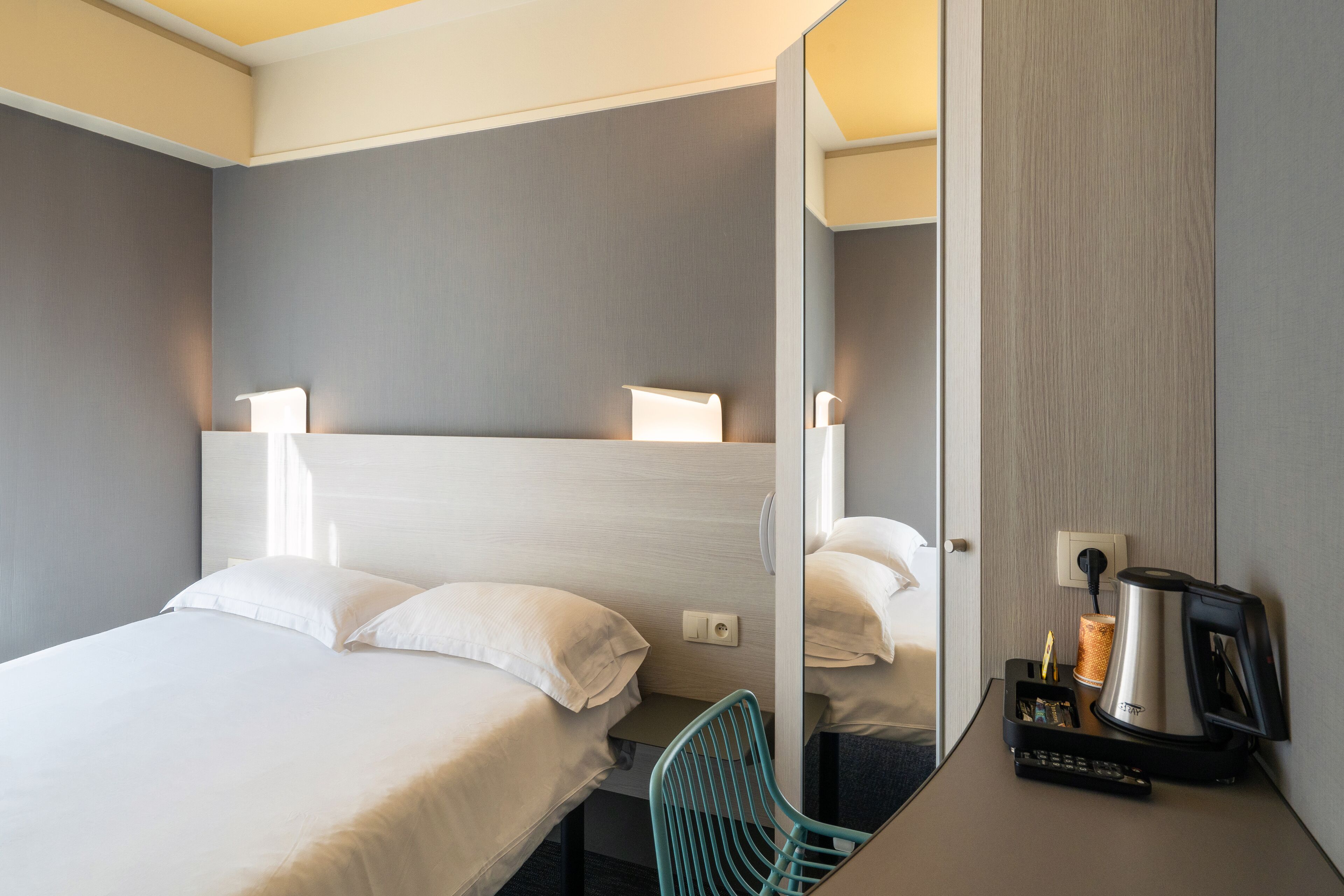Habitación de hotel con cama, escritorio con cafetera, silla y espejo.