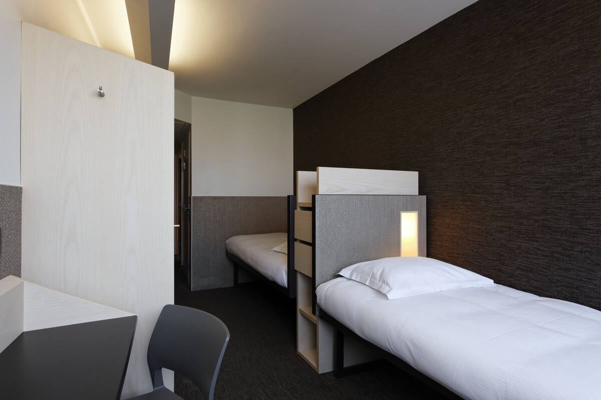 A modern hotel room with a bunk bed, a desk, and a chair.