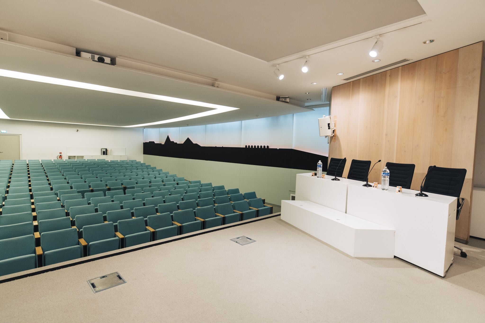 Un salón de conferencias con filas de sillas, un atril blanco y un revestimiento de pared de madera.