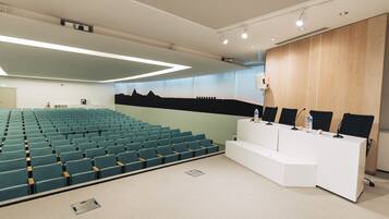 Un salón de conferencias con filas de sillas, un atril blanco y un revestimiento de pared de madera.