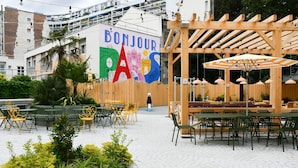 Un espace extérieur aménagé avec des tables et des chaises, une pergola en bois et une enseigne indiquant « BONJOUR ».