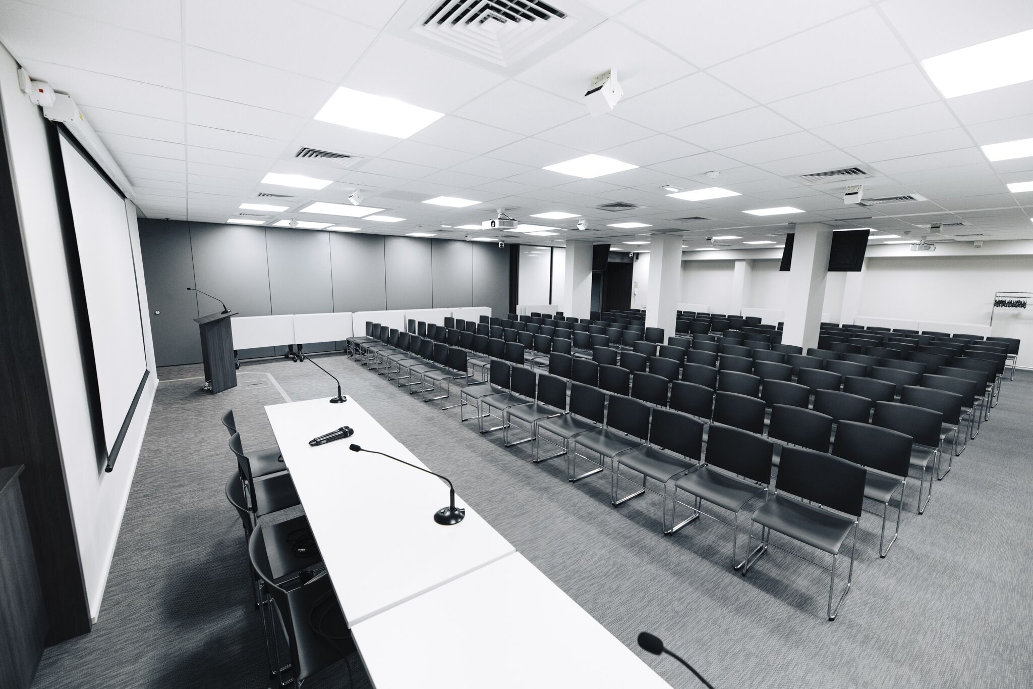 Une salle de conférence avec des rangées de chaises, un pupitre et un écran de projection.