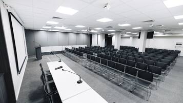 Une salle de conférence avec des rangées de chaises, un pupitre et un écran de projection.