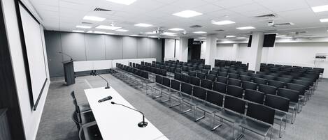 Ein Konferenzraum mit Reihen von Stühlen, einem Rednerpult und einer Projektionsleinwand.