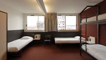 A hotel room with two single beds, a desk, a chair, and a window with curtains.