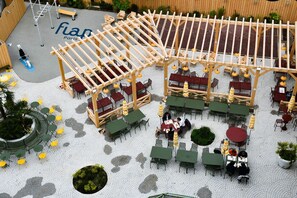 An outdoor café with wooden pergolas, green tables, and yellow umbrellas. - FIAP - Hostel (Paris)