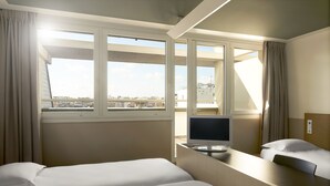 Une chambre d’hôtel avec deux lits, un bureau avec une télévision et une grande fenêtre donnant sur la ville.