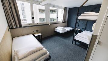Une chambre d’hôtel avec un lit superposé, un lit simple, une petite table et une fenêtre avec des rideaux.