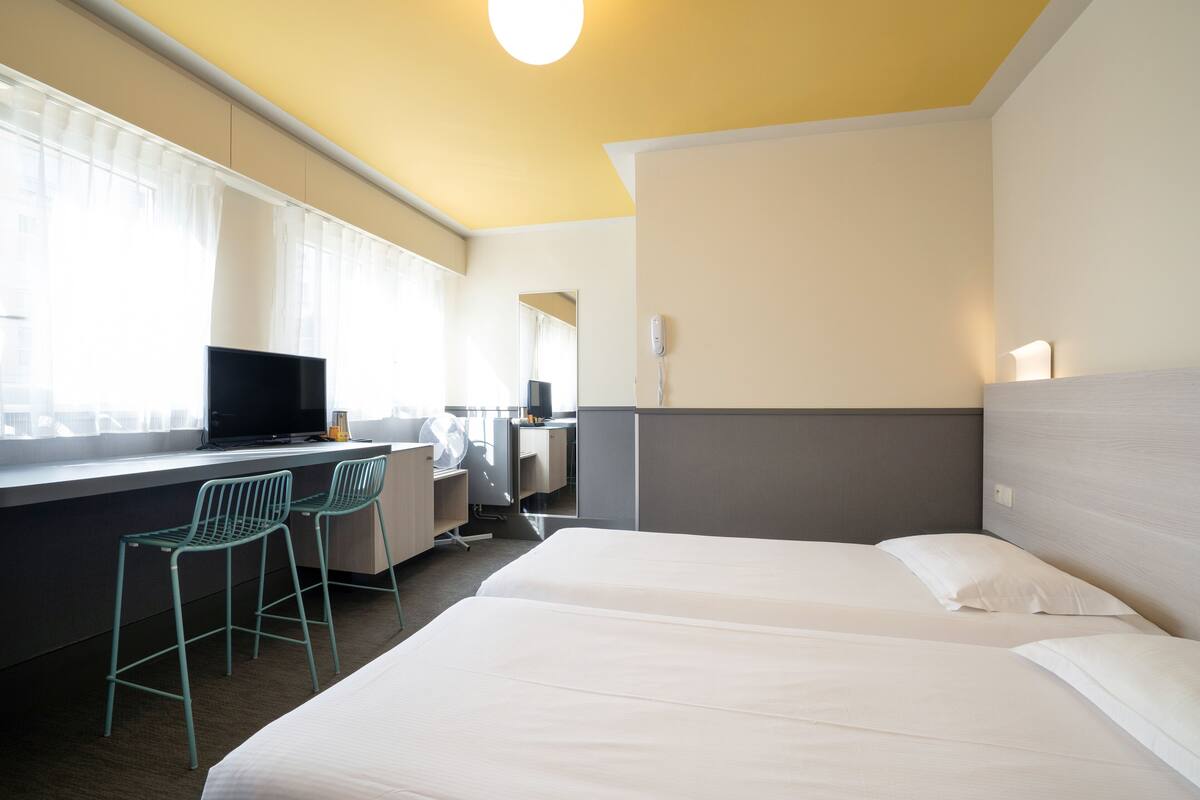 A hotel room with two beds, a desk with a computer, and two chairs.