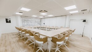 Une salle de conférence avec une longue table et des chaises, des murs blancs et un plancher en bois.