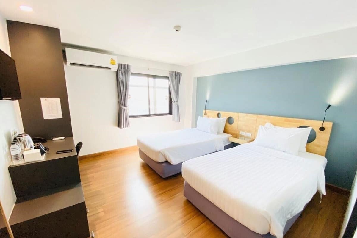 A hotel room with two beds, a desk, and a window with curtains.