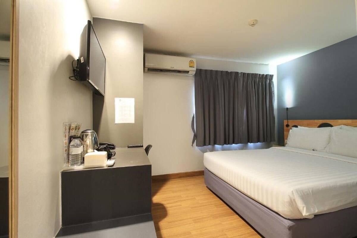 A hotel room with a bed, a desk with a telephone, a coffee maker, and an air conditioning unit.