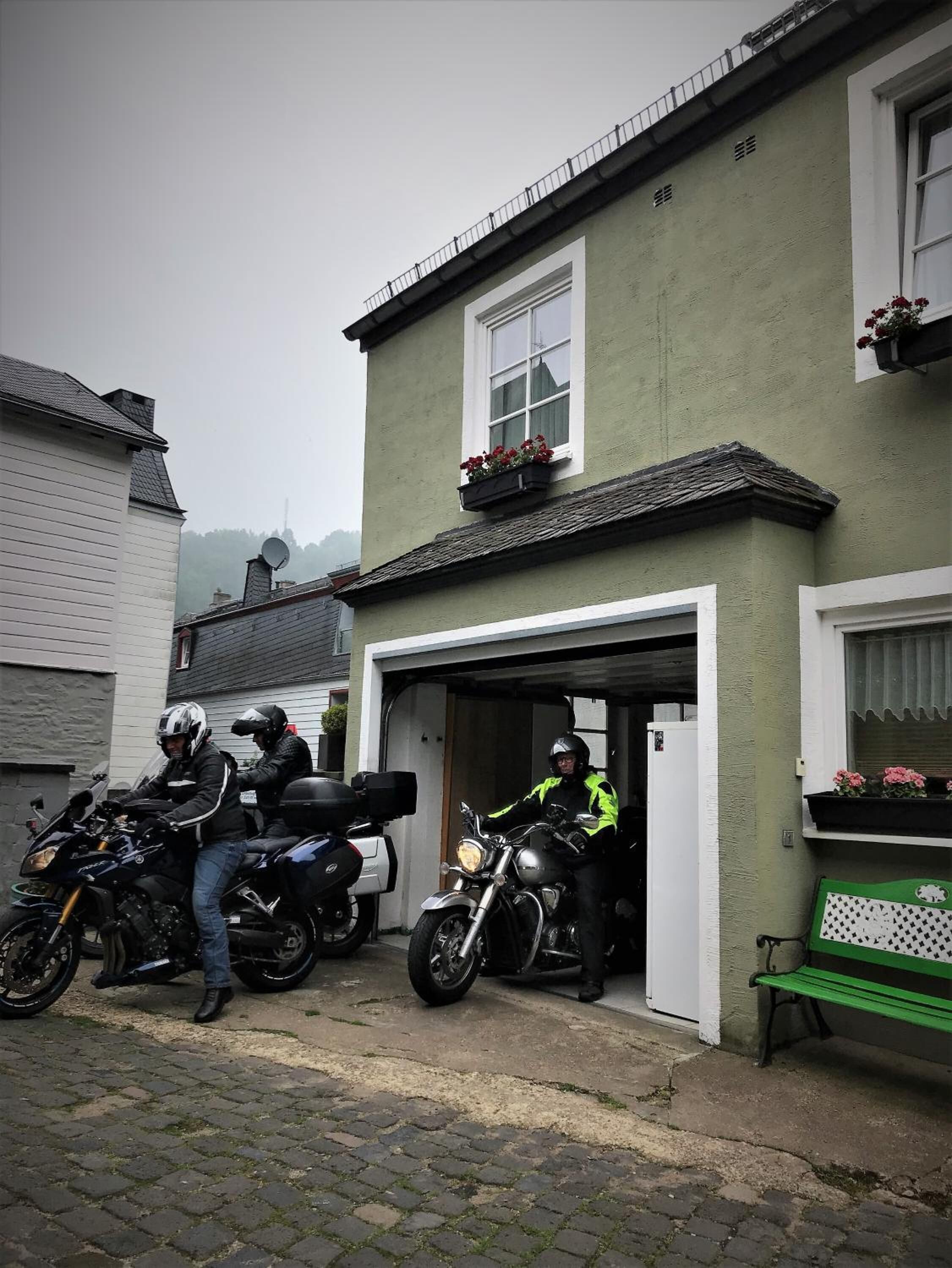 Een gebouw met een open garagepoort, geparkeerde motorfietsen en een bank buiten.
