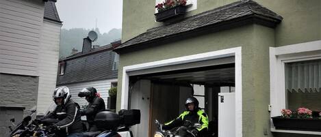 Un edificio con una puerta de garaje abierta, motocicletas estacionadas y un banco en el exterior.