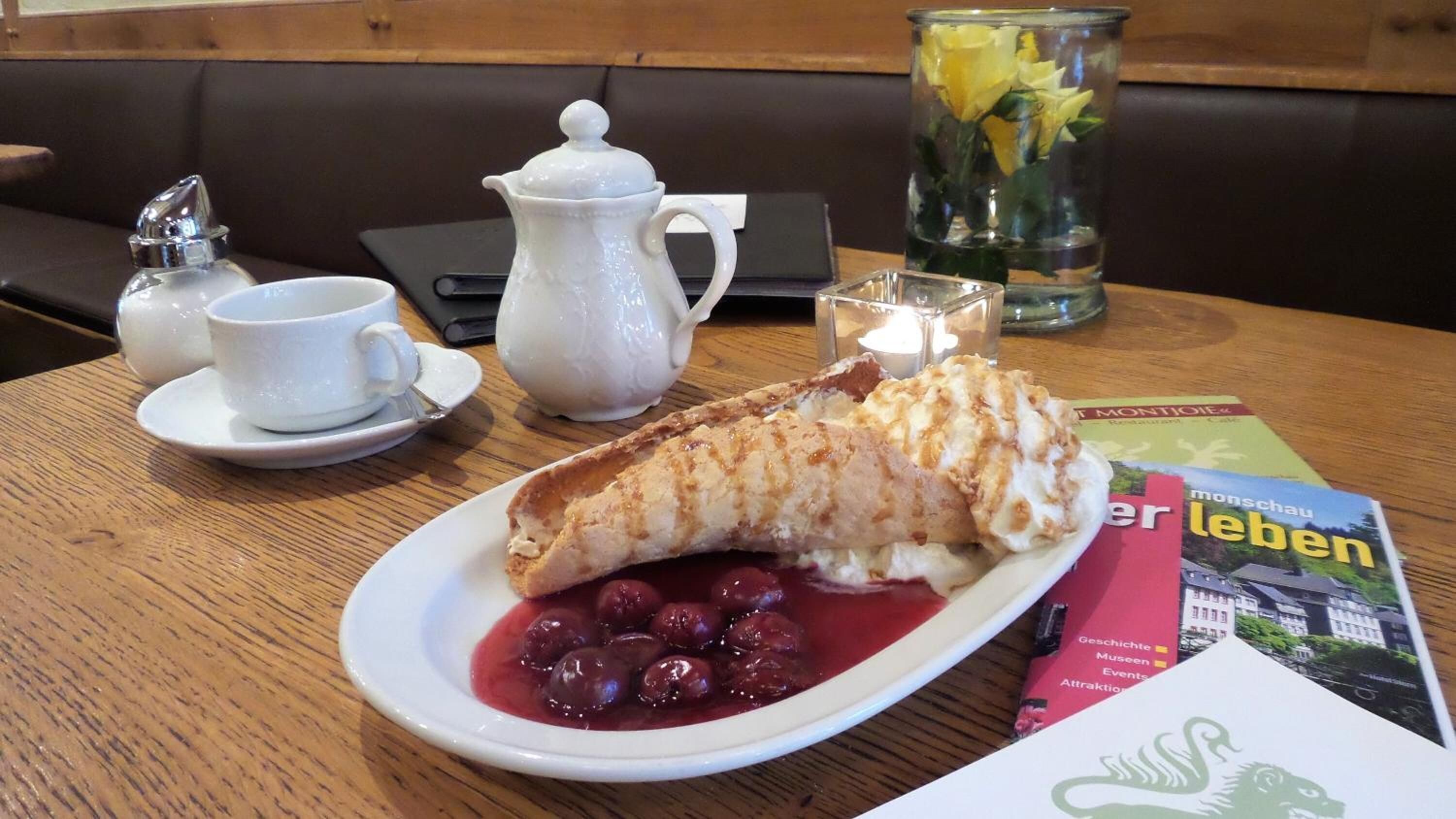 Un plato de postre con un pastel, cerezas y un vaso de agua sobre una mesa.